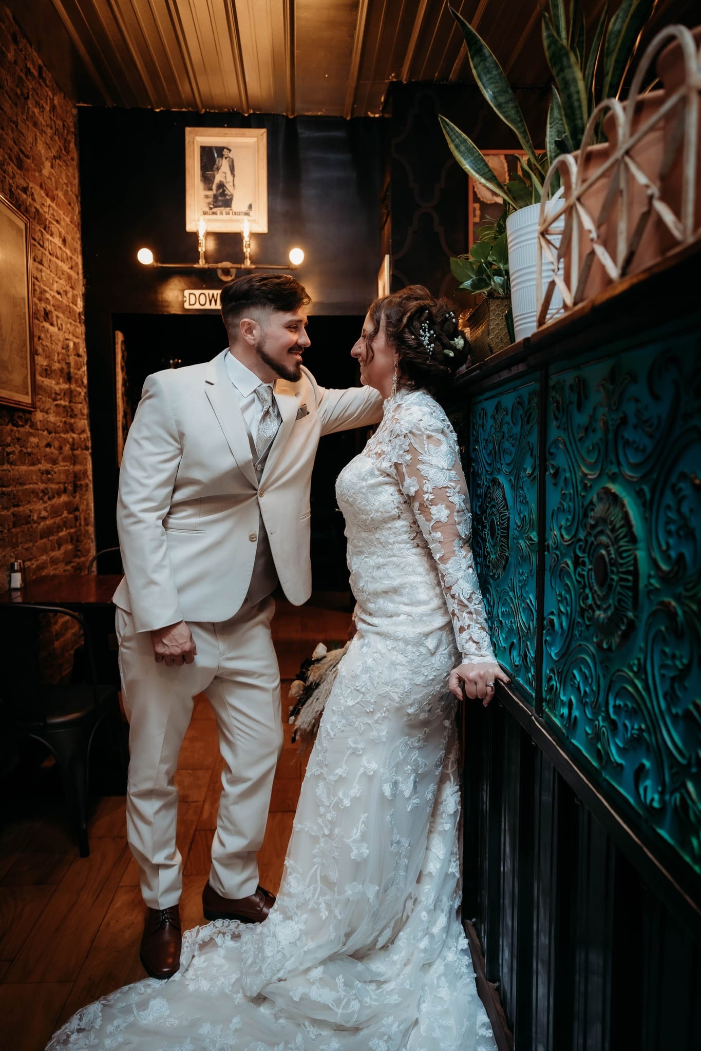 Wedding couple smiling at each other beside an ornate teal railing indoors.